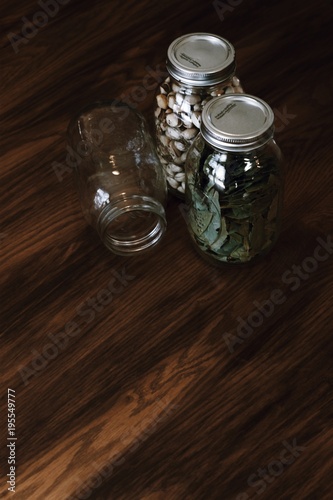 Mason jars with pistachios and bay leaves on dark, wooden table