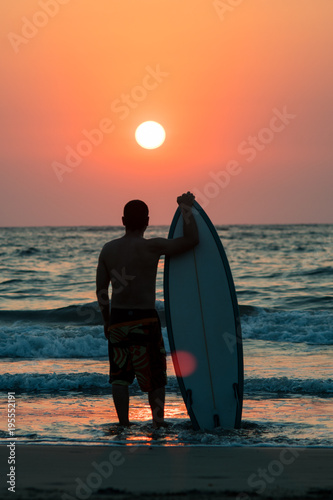 surfer walking on beach at sunset