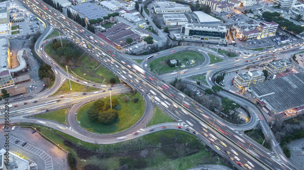Aerial view of a stretch of highway in the Italian countryside on a cloudy night. The road is divided into three lanes in each direction. There are cars and trucks on the street. Aerial view of a stretch of highway in the Italian countryside on a cloudy night. The road is divided into three lanes in each direction. There are cars and trucks on the street.