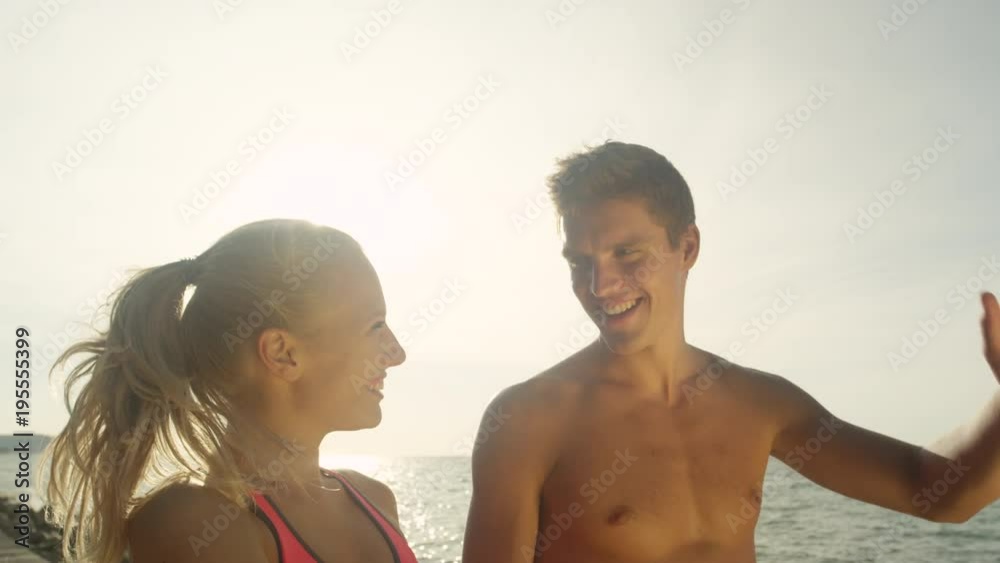 SLOW MOTION, CLOSE UP, LENS FLARE: Bright summer sun illuminates victorious couple high fiving by the sea. Supportive girlfriend and boyfriend celebrate their successful workout with a high five. SLOW MOTION, CLOSE UP, LENS FLARE: Bright summer sun illuminates victorious couple high fiving by the sea. Supportive girlfriend and boyfriend celebrate their successful workout with a high five.