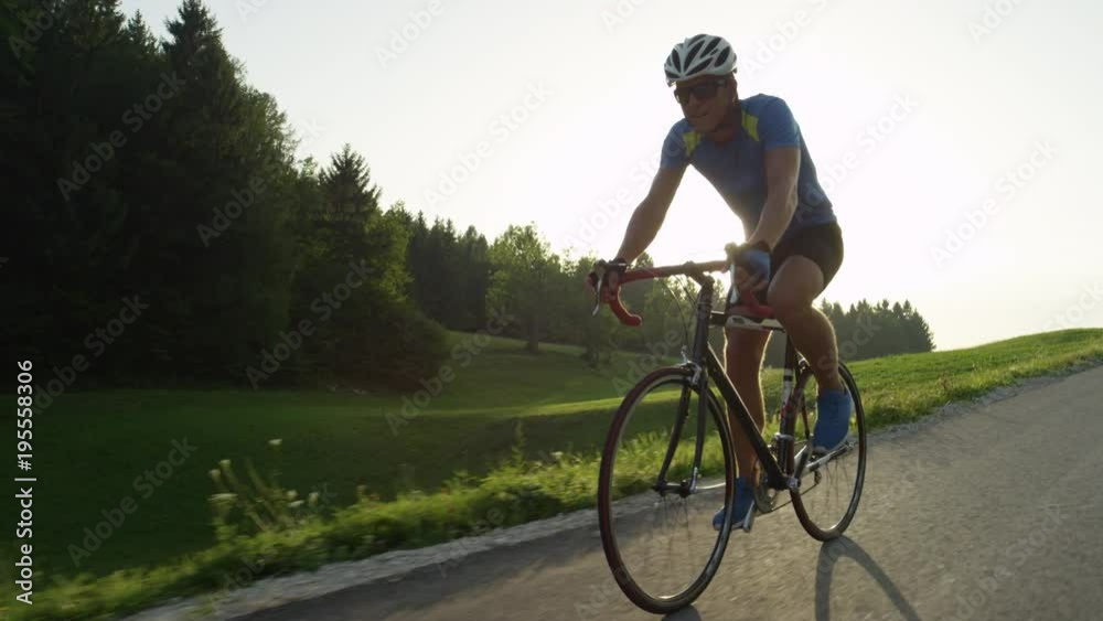 SLOW MOTION, SUN FLARE: Pro cyclist easily overtakes moving camera on beautiful summer evening. Biker man with sunglasses pedaling hard towards the finish line of road trial across the countryside. SLOW MOTION, SUN FLARE: Pro cyclist easily overtakes moving camera on beautiful summer evening. Biker man with sunglasses pedaling hard towards the finish line of road trial across the countryside.