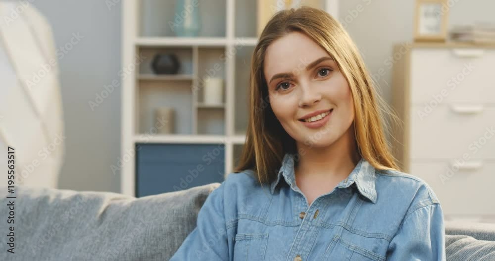 Close up of the charming young woman turning her head and smiling at the camera in the cozy living room. Inside. Portrait Close up of the charming young woman turning her head and smiling at the camera in the cozy living room. Inside. Portrait