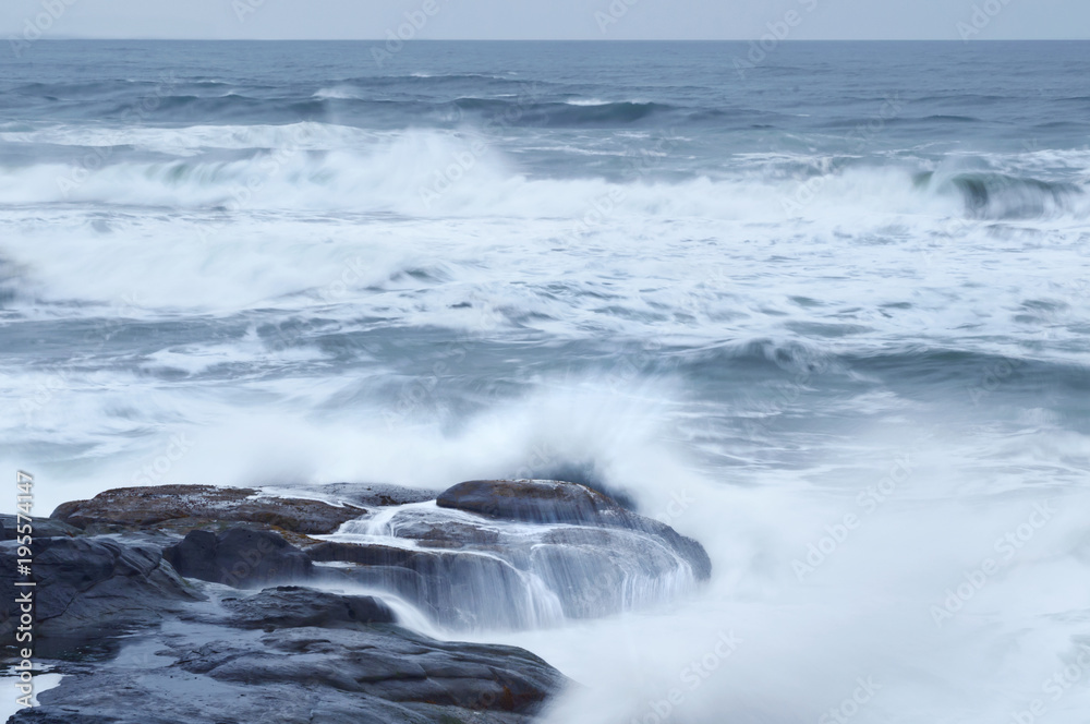 Rocky ocean beach landscape with crashing ocean waves spilling on rocks
