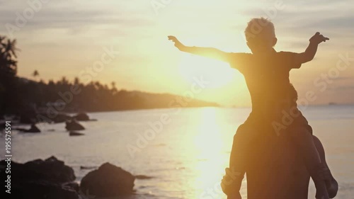 Happy father and son in eyeglasses playing on tropical beach boy rising up hands imitating a flight at wonderful sunset in slow motion. 3840x2160