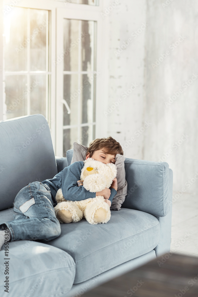 Sweet dreams. Adorable little fair-haired boy hugging his favourite nice toy and lying on the sofa while taking a nap Sweet dreams. Adorable little fair-haired boy hugging his favourite nice toy and lying on the sofa while taking a nap