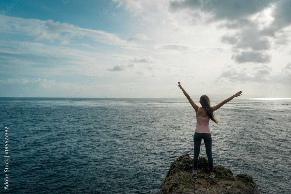 Woman with raised arms standing on ocean cliff and feeling free. Bali, Indonesia Woman with raised arms standing on ocean cliff and feeling free. Bali, Indonesia