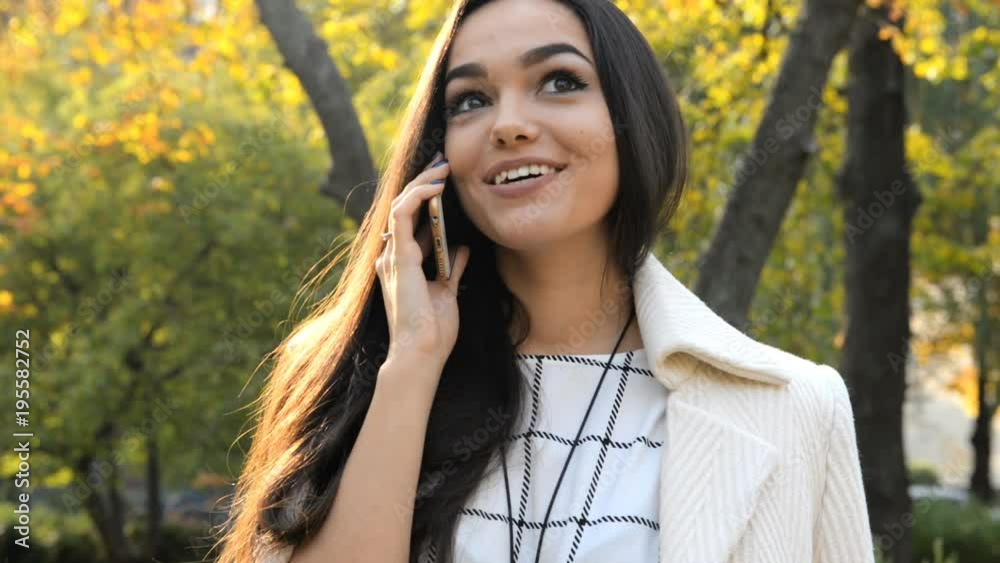 Young beautiful brunette is standing near a tree in the street and talking on the phone. Young beautiful brunette is standing near a tree in the street and talking on the phone.