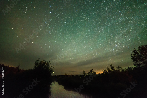 Stars and night sky over a small lake with fireflies