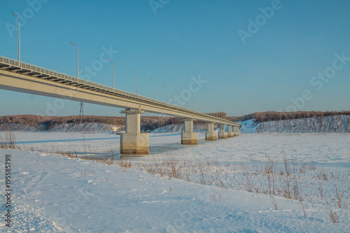 a bridge across a river covered with ice and snow on winter sunny day © kapichka