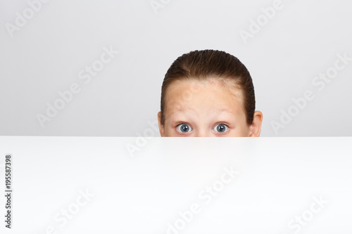 A little girl with fear in her eyes is hiding under the table.