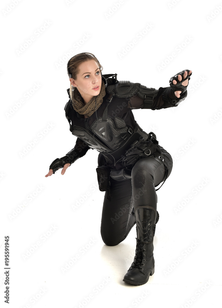 full length portrait of female  soldier wearing black  tactical armour, seated pose, isolated on white studio background.
