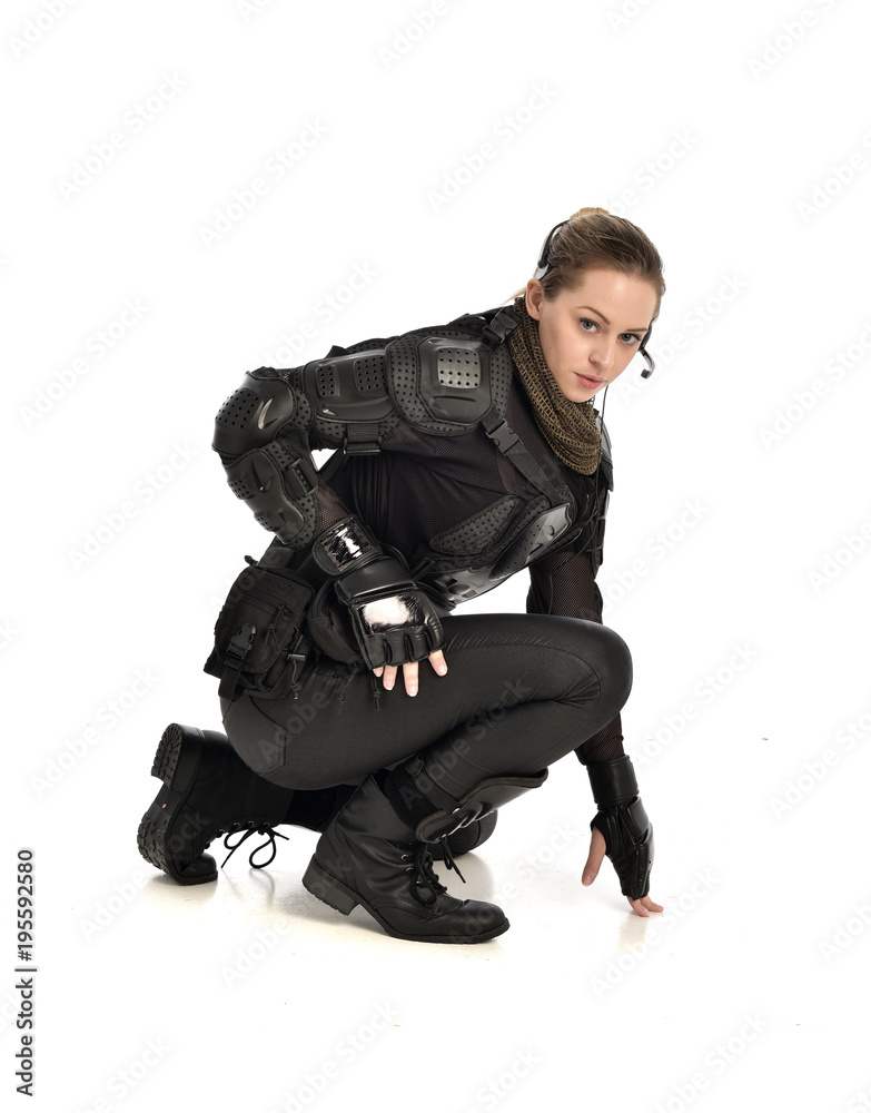 full length portrait of female  soldier wearing black  tactical armour, seated pose, isolated on white studio background.