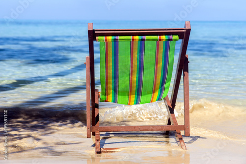 Empty lounger on the sea beach. Colorful chair stands abandoned on a sunny seashore. Vacation on a tropical island.