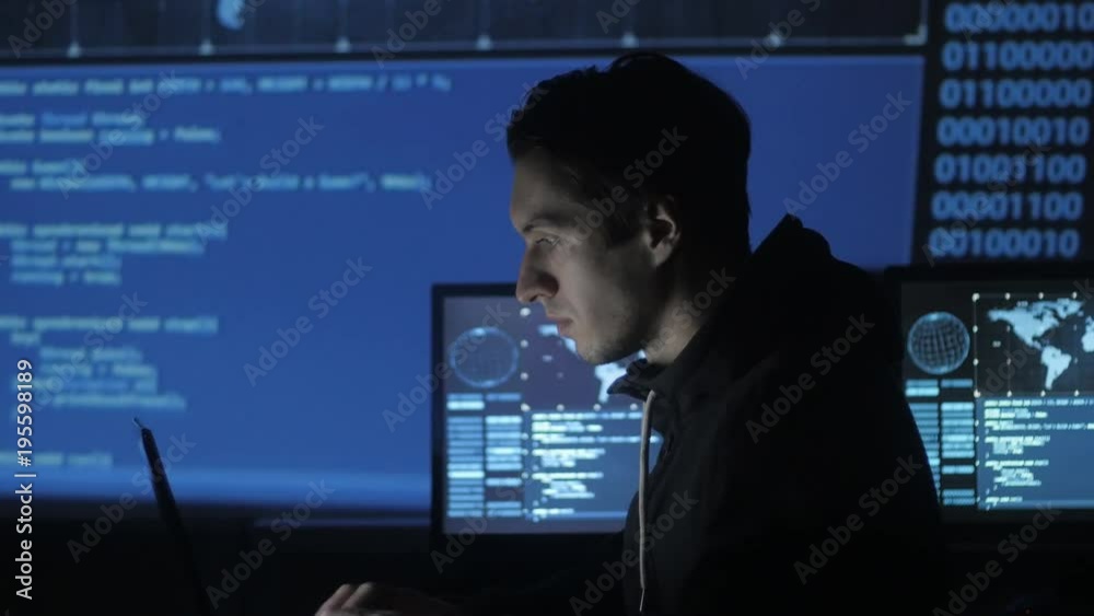 Geek Hacker programmer is working on computer in cyber security center filled with display screens. Geek Hacker programmer is working on computer in cyber security center filled with display screens.