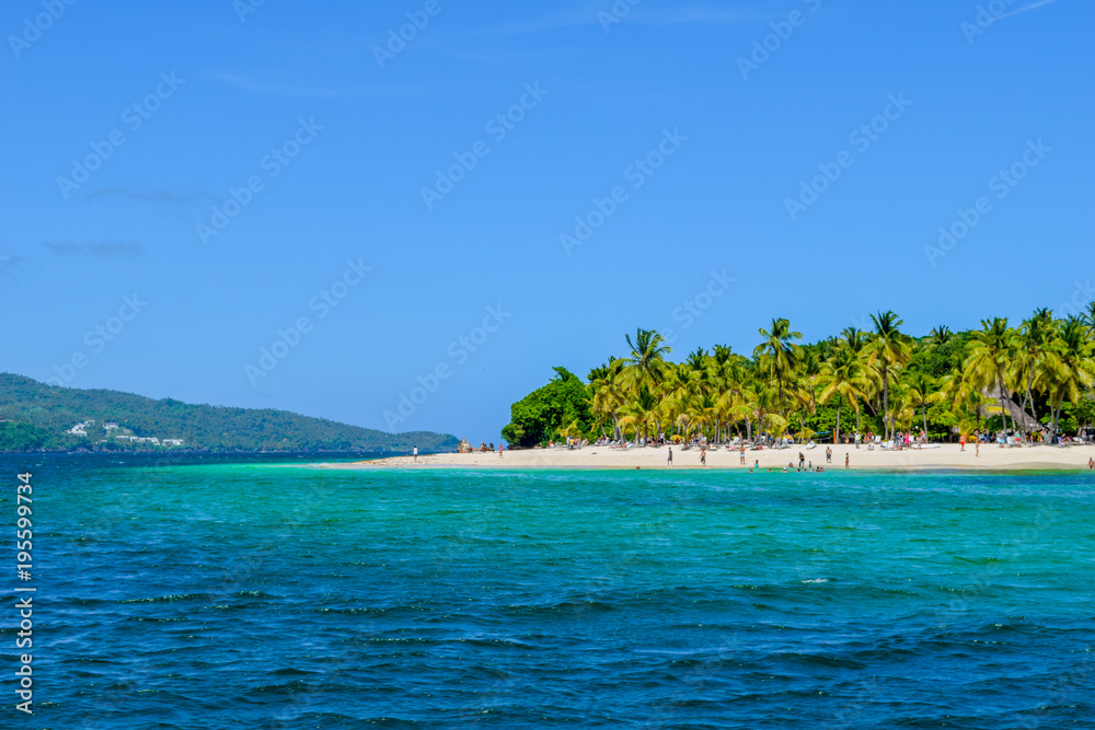 Beautiful beach with palms, blue sky and turquoise water, some tourists having fun, relaxing and swimming in the ocean, caribbean sea