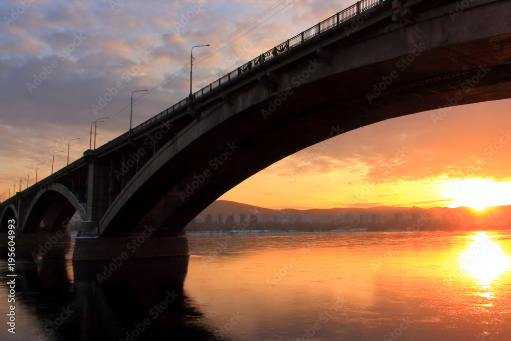 Winter golden sunset over the Yenisei river in Krasnoyarsk. The sun is reflected in the mirror-like surface of the water Winter golden sunset over the Yenisei river in Krasnoyarsk. The sun is reflected in the mirror-like surface of the water