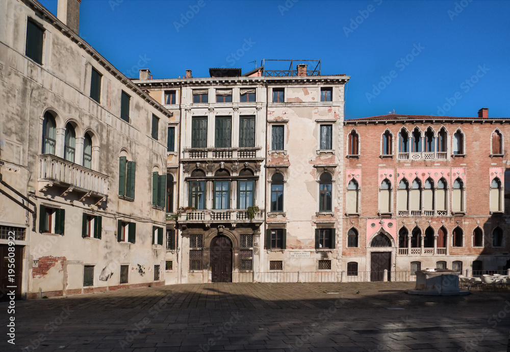 historic Venetian residences in a sunny square with a well and the tables of a cafe. Venice, Italy