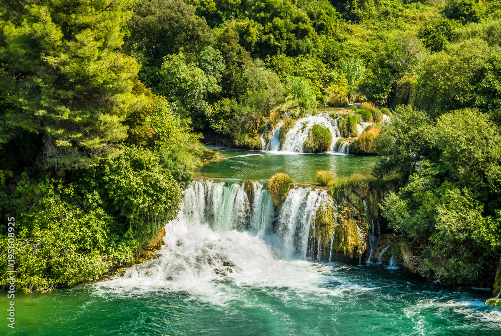 Fototapeta premium Piękny wodospad wśród zielonych drzew. Krajobraz w paku Krka w Chorwacji.