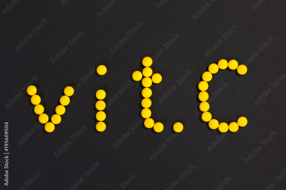 Top view of  inscription “vit. C” made of yellow pills on black background.
