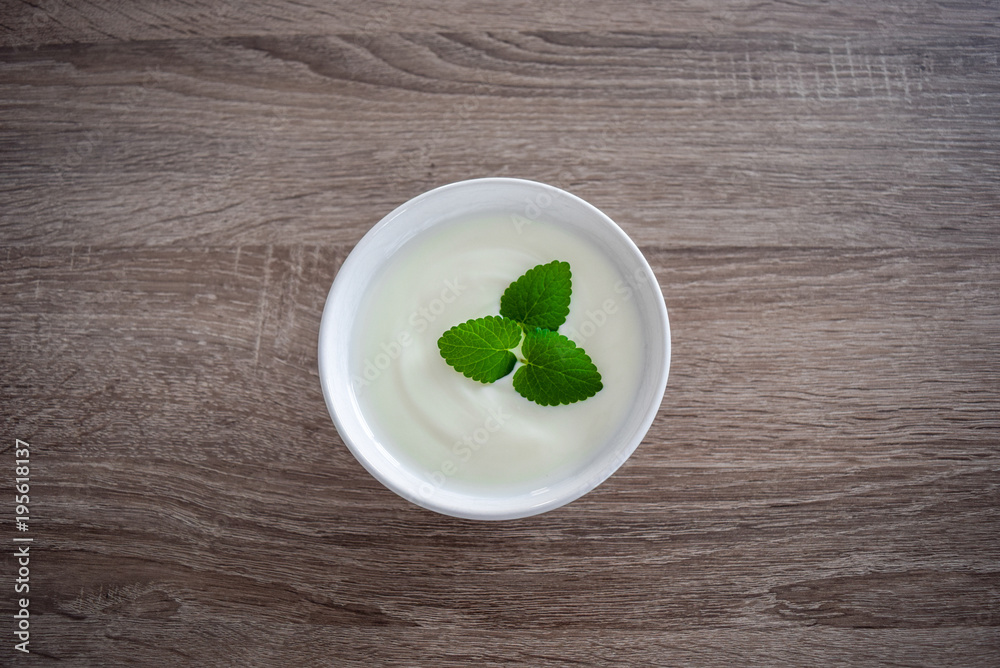 Ceramic bowl of white yogurt with mint leaves as decoration isolated on vintage rustic wooden table from top view, plain yoghurt Ceramic bowl of white yogurt with mint leaves as decoration isolated on vintage rustic wooden table from top view, plain yoghurt