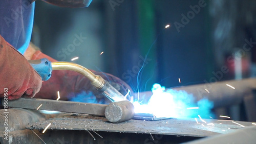 Fototapeta Naklejka Na Ścianę i Meble -  Worker with protective mask welding metal. A man welds a metal with a welding machine. Welder is working at the factory and welding a metal construction. Welders working at the factory made metal