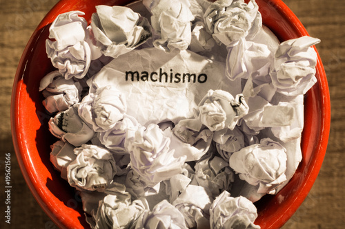 Crumpled paper written machismo, portuguese and spanish word for chauvism, inside the trash can. Paper balls. Concept of old and abandoned idea or practice.