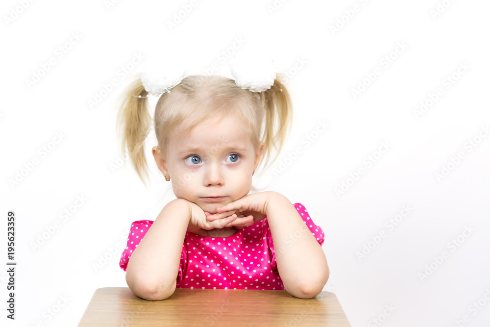 A beautiful young blond girl leans her elbows on a chair and puts her head on her hands. Little girl 3 years old on a white background put her head on her hands. A beautiful young blond girl leans her elbows on a chair and puts her head on her hands. Little girl 3 years old on a white background put her head on her hands.