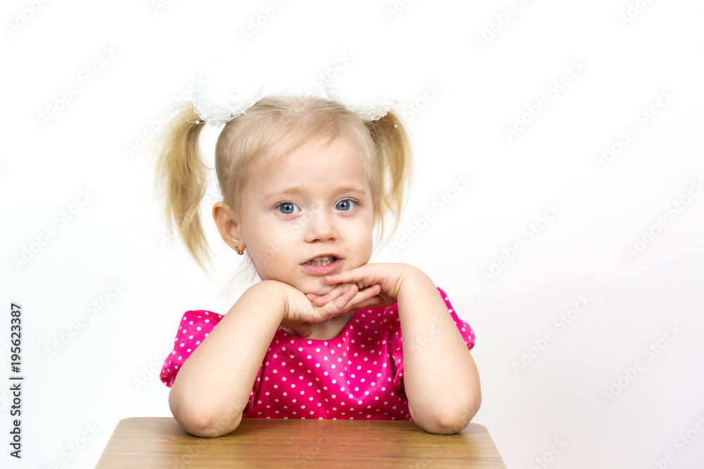 A beautiful young blond girl leans her elbows on a chair and puts her head on her hands. Little girl 3 years old on a white background put her head on her hands. A beautiful young blond girl leans her elbows on a chair and puts her head on her hands. Little girl 3 years old on a white background put her head on her hands.