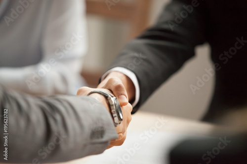 Two businessmen in suits shaking hands at group meeting, partners handshaking at negotiations making deal or signing contract, thanking for help support, welcome greeting handshake concept, close up