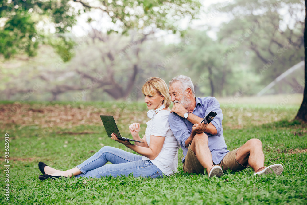Elderly couple using a laptop while sitting on grass in the park Elderly couple using a laptop while sitting on grass in the park