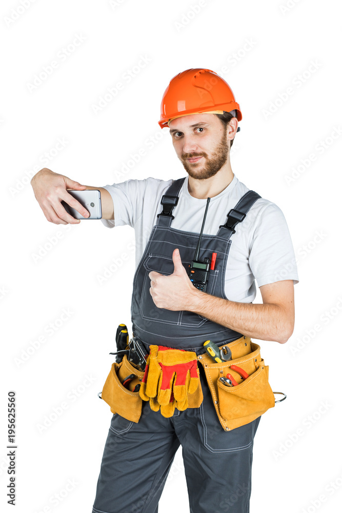 Smiling young construction worker showing a sign and taking a picture from the phone. Repair and construction. Isolated on white background Smiling young construction worker showing a sign and taking a picture from the phone. Repair and construction. Isolated on white background