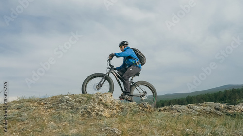 Fat bike also called fatbike or fat-tire bike in summer driving through the hills. The guy is riding a bike along the sand and grass high in the mountains. He performs some tricks and runs dangerously