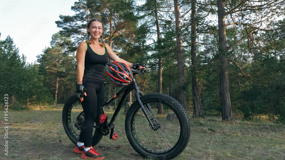 Fototapeta premium Fat bike also called fatbike or fat-tire bike in summer riding in the forest. Beautiful girl and her bicycle in the forest. She rolls her bike and poses to the operator.