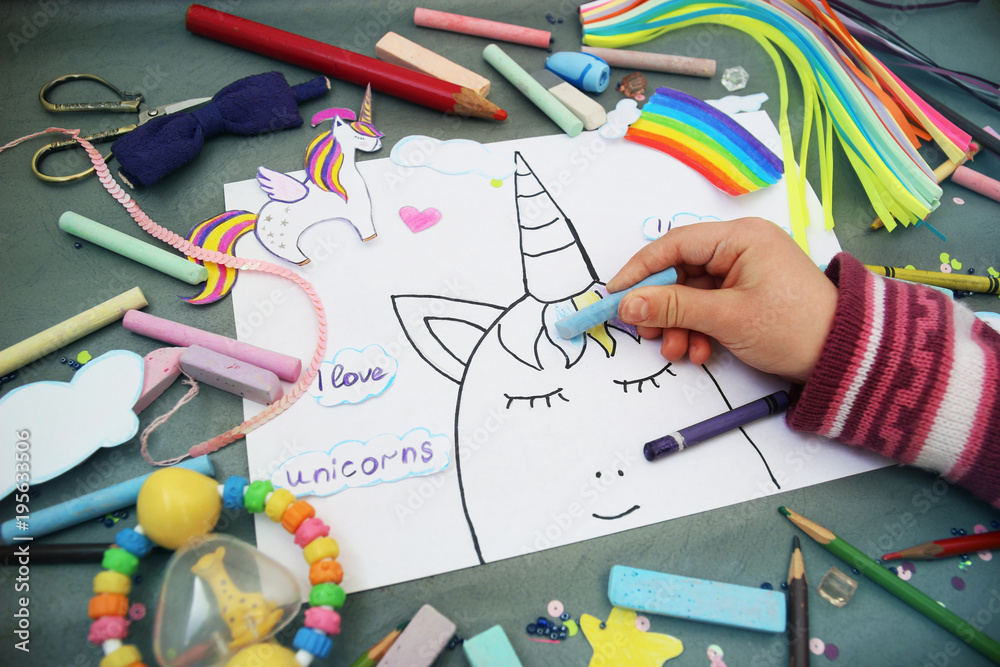 The child draws the unicorn's face with colored pencils on a gray background The child draws the unicorn's face with colored pencils on a gray background