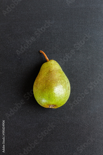 Single fresh green pear on black chalkboard background