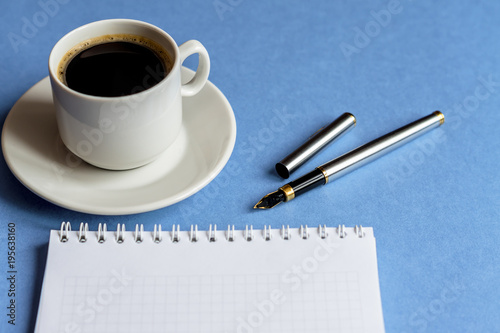 cup of black coffee with notebook and pen on light blue background. business concept with copy space