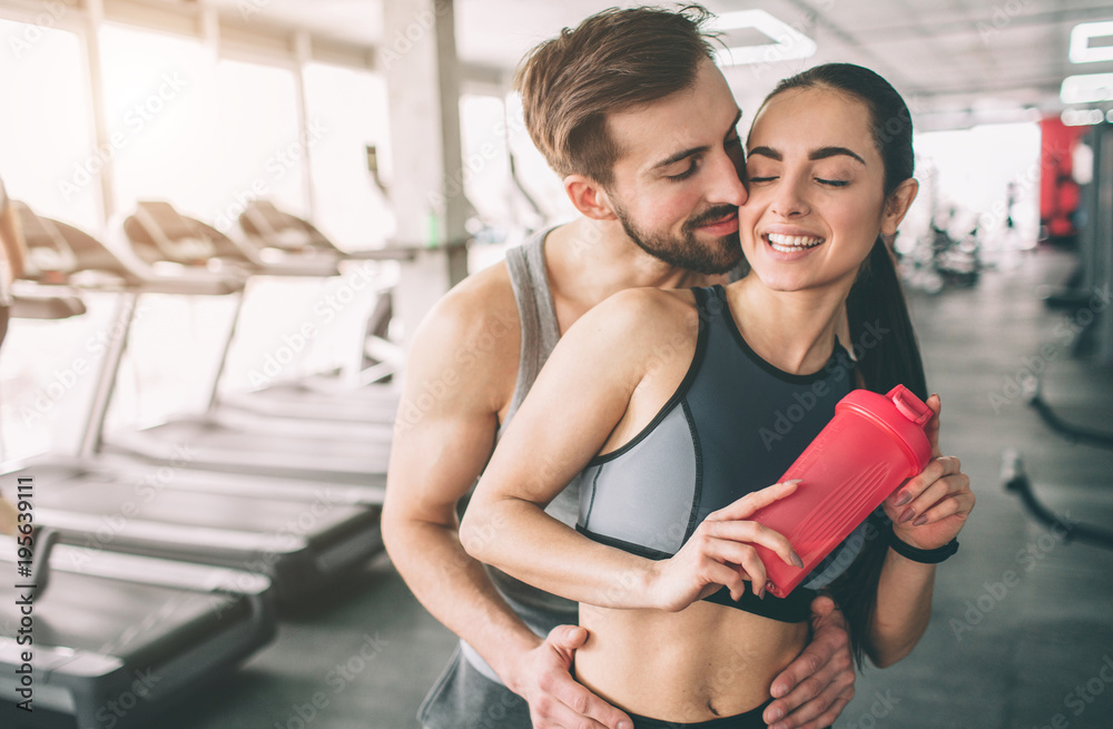 Amazing couple standing in the gym. The guy is hugging his girlfriend. She looks happy. Close up. Cut view. Amazing couple standing in the gym. The guy is hugging his girlfriend. She looks happy. Close up. Cut view.