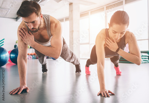 Slim girl and strong man are standing in one hand plank position and balancing on that hand. They look concentrated and concious.