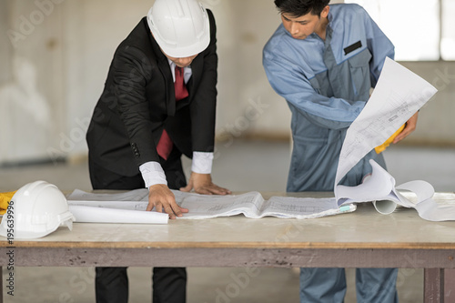 Business man is wear white helmet stand with engineer.They are looking at blueprint on the table. photo