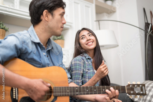 In selective focus of Young beautiful couple resting at home and playing guitar.Handsome man palying Guitar for his girlfriend learning to sing a song.