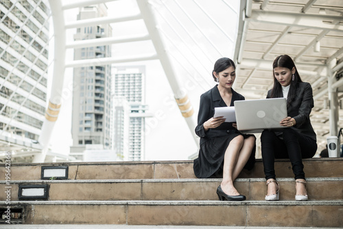 two business women sit on the staircase and talk about business with laptop and copy space for text