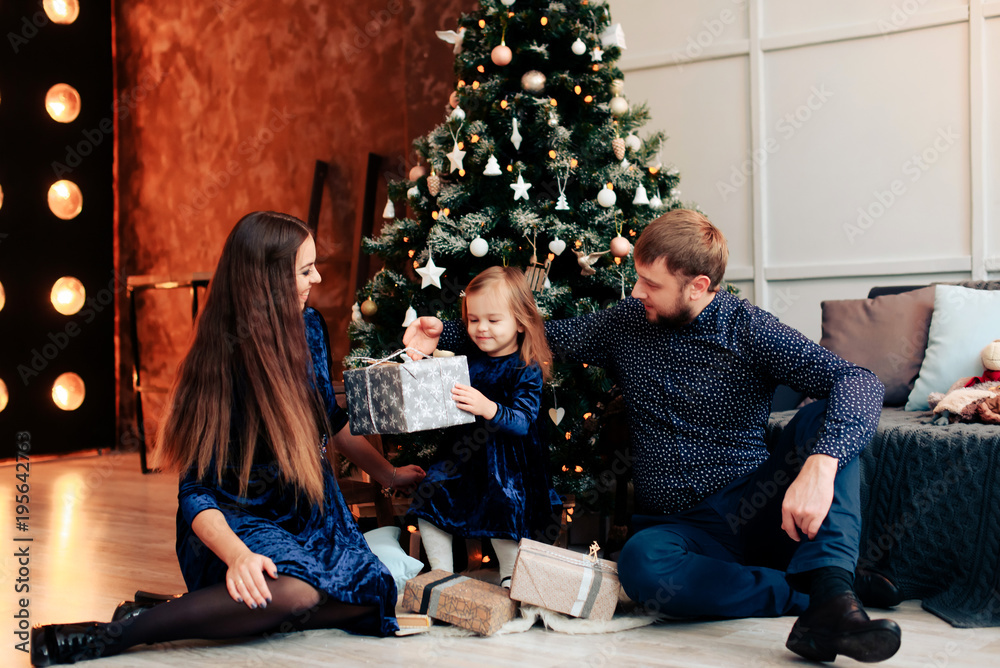 young mother and father and their little daughter in a New Year decor with gifts and a Christmas tree young mother and father and their little daughter in a New Year decor with gifts and a Christmas tree