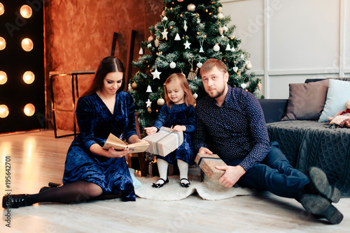 young mother and father and their little daughter in a New Year decor with gifts and a Christmas tree photo