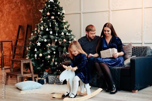 young mother and father and their little daughter in a New Year decor with gifts and a Christmas tree photo