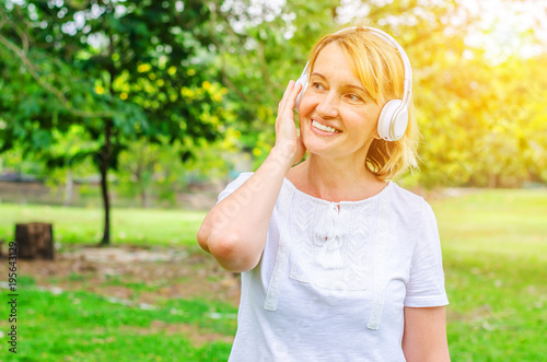 blonde senior woman listening to music in nature, woman listening music radio with wireless headphones on mobile cheerful in park, Happy life concept