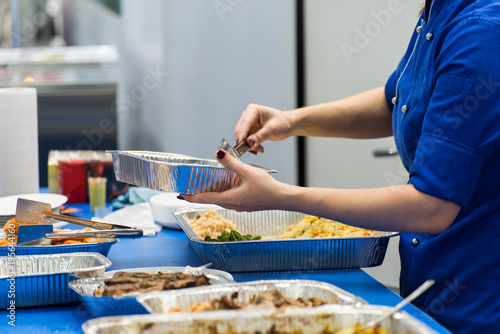 cook in a blue uniform puts a salad in a tray closeup