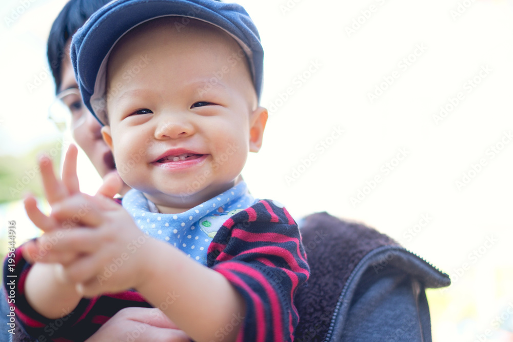 Asian Father holding Happy toddler baby boy smiling wearing sweater, bib, hat clapping hands at garden outdoors, Dad and son who is mouth open showing first teeth, Happy kid concept with copyspace Asian Father holding Happy toddler baby boy smiling wearing sweater, bib, hat clapping hands at garden outdoors, Dad and son who is mouth open showing first teeth, Happy kid concept with copyspace