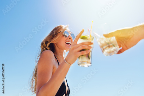 Photography Smiling pretty woman with long hair in swimsuit and sunglasses, drinking a cocktail, toasting, celebrating something with friend, spending vacation on the beach, at sunny day
