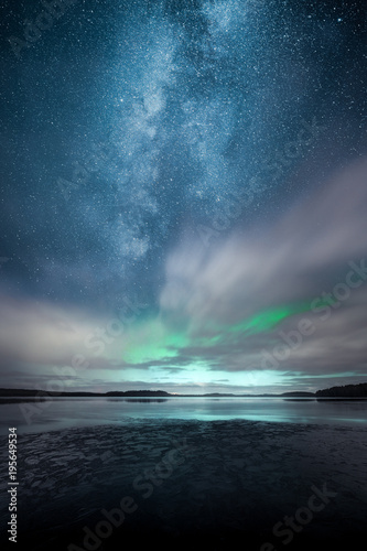 Northern Lights aka Aurora Borealis behind fast moving clouds with reflections on lake