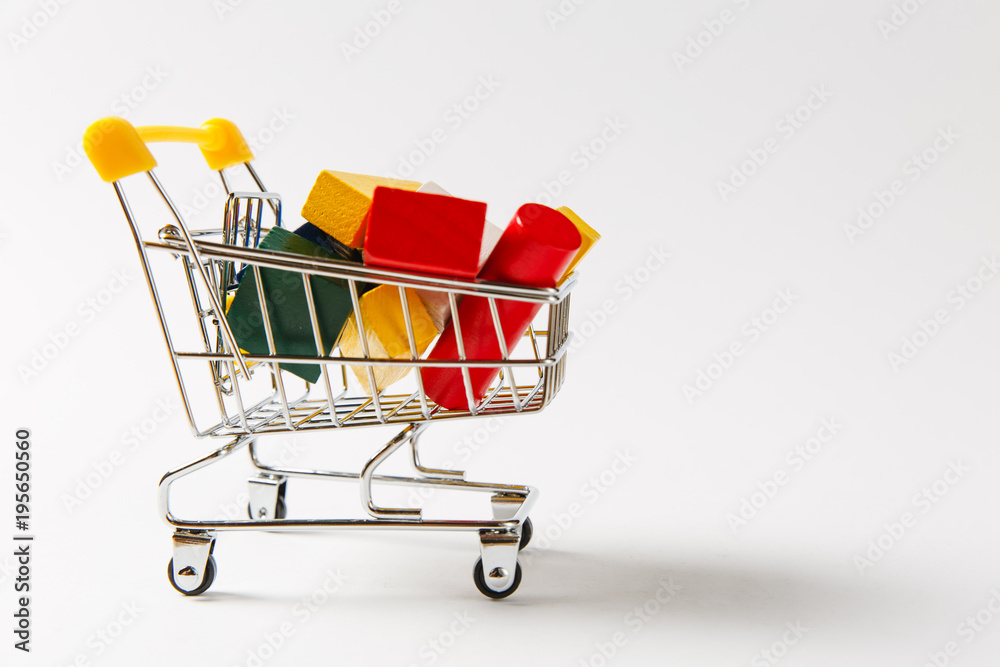 Close up of supermarket grocery push cart for shopping with yellow handle filled with multi-colored geometric shapes isolated on white background. Concept of shopping. Copy space for advertisement